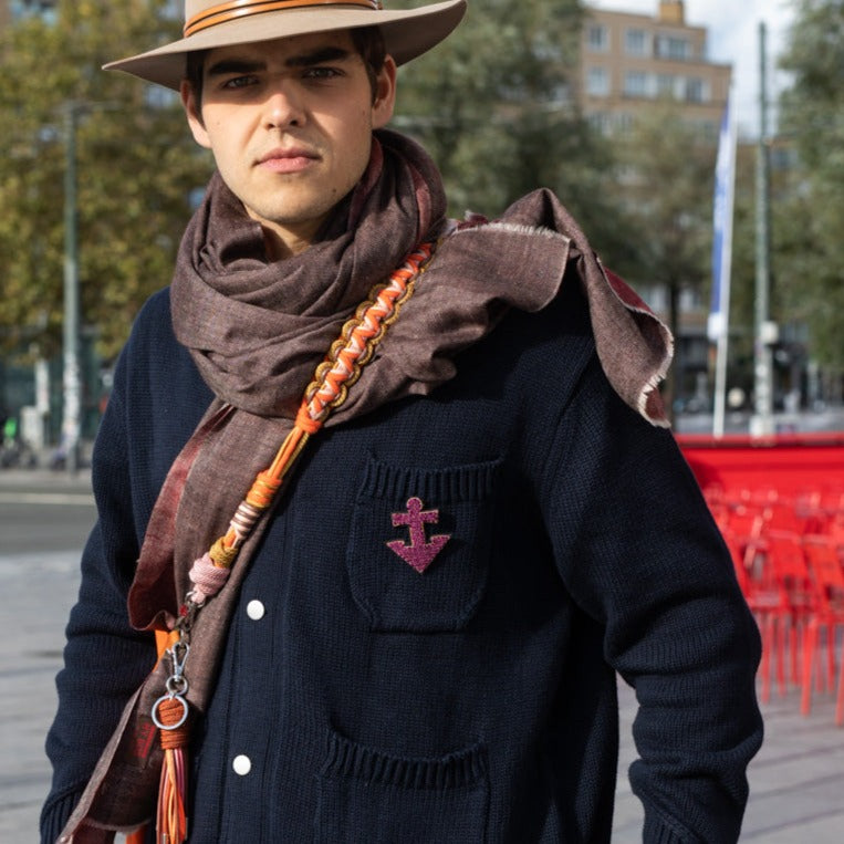 An embroidered brooch representing an purple anchor worn by a model.