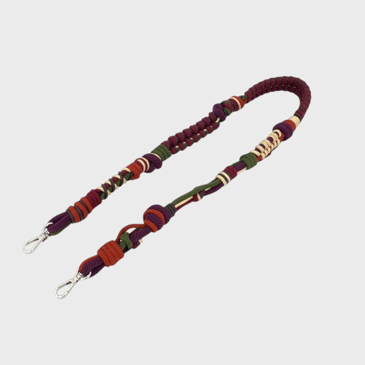 Multicolored braided macramé bag strap in dark green, purple, and orange, shown on a light gray background.
