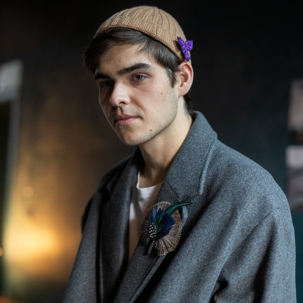 A person wearing a gray cashmere beanie with a colorful fly pin attached to it.