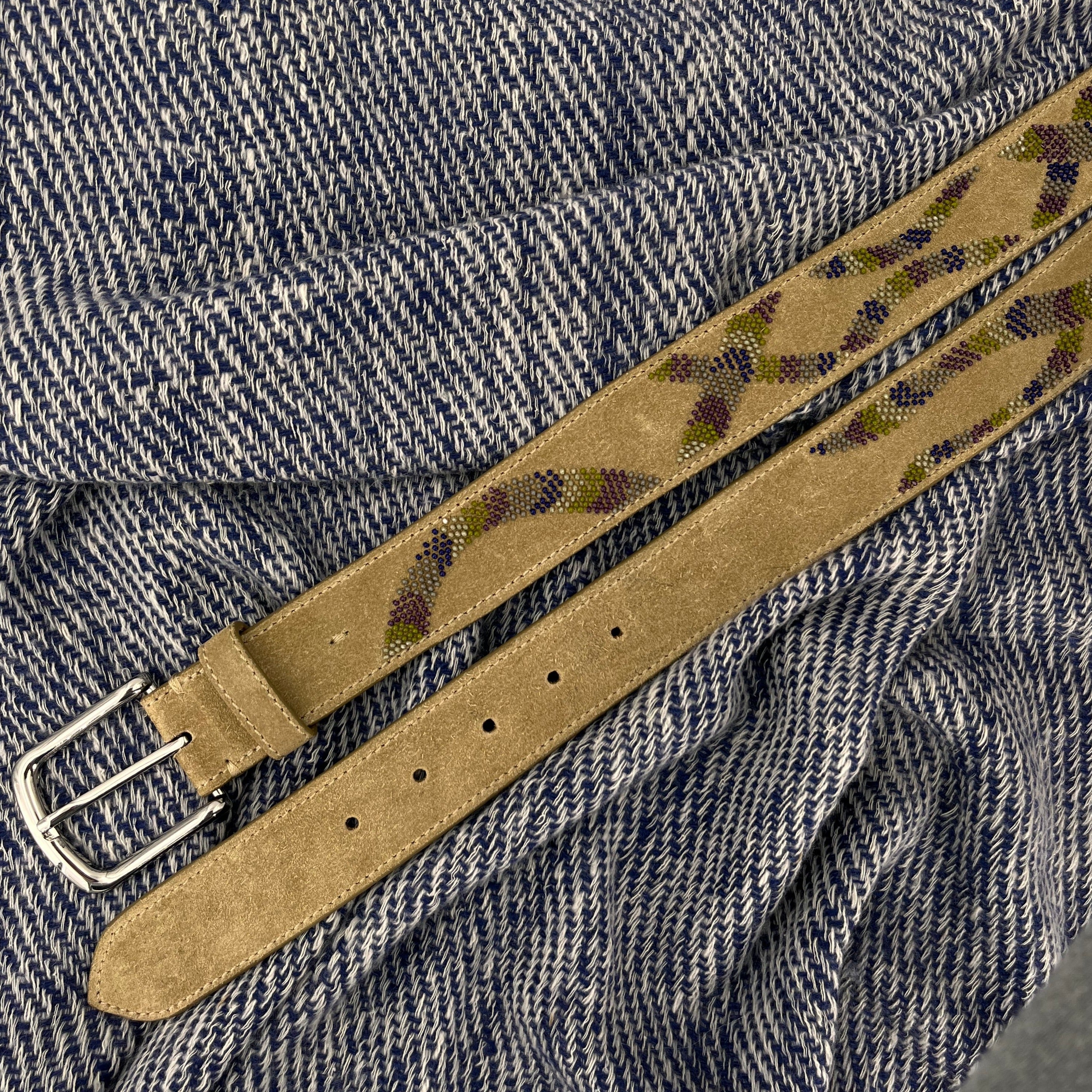 Beige suede belt with a silver buckle and a colourful embroidered snake pattern on a blue and white bed cover.