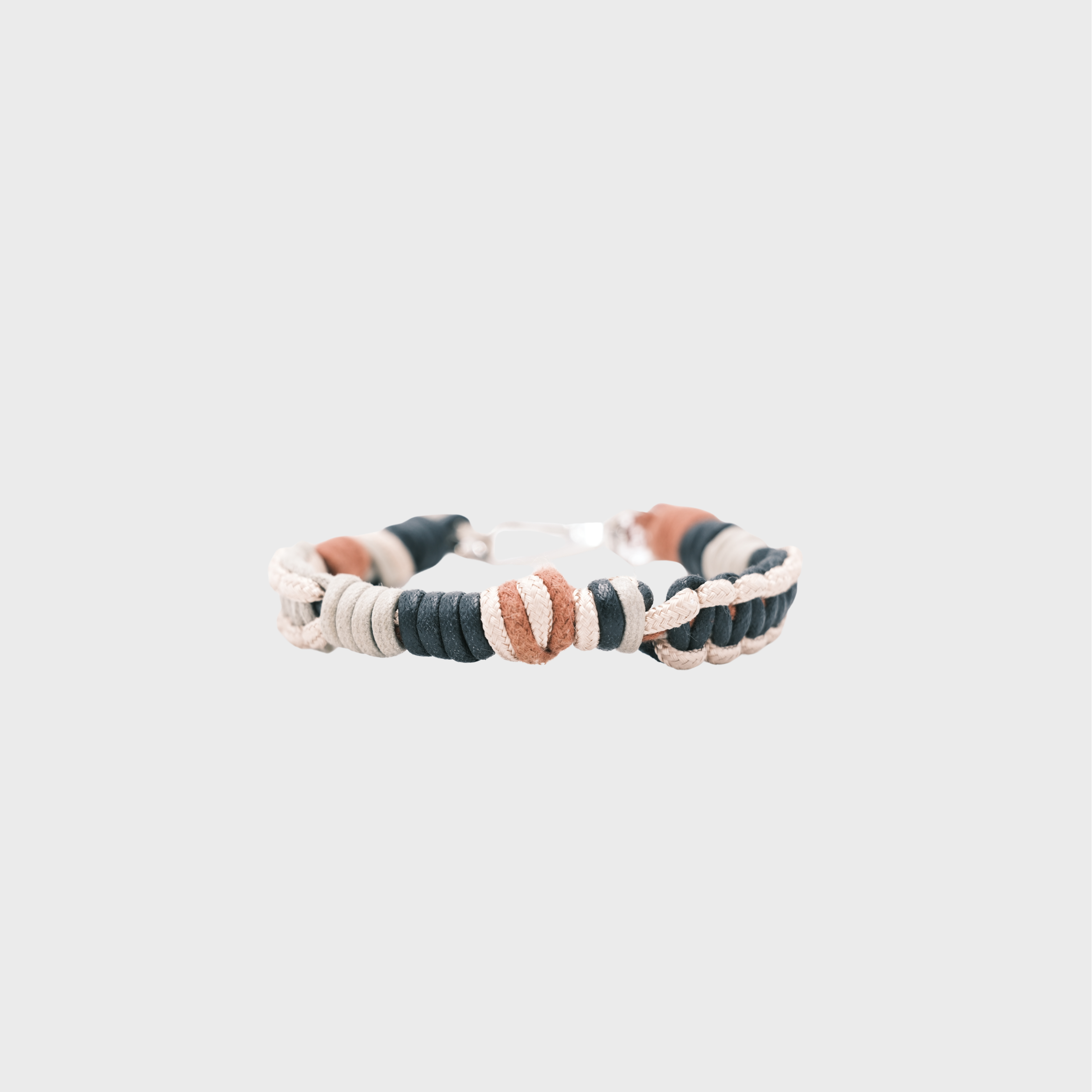 A handmade braided macramé cord collar in white, beige, black and brown with a silver clasp, centered on a light gray background.