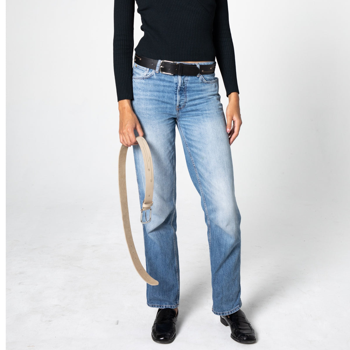 Person wearing blue jeans and a black top and a black leather belt with small stitched lines on a white background