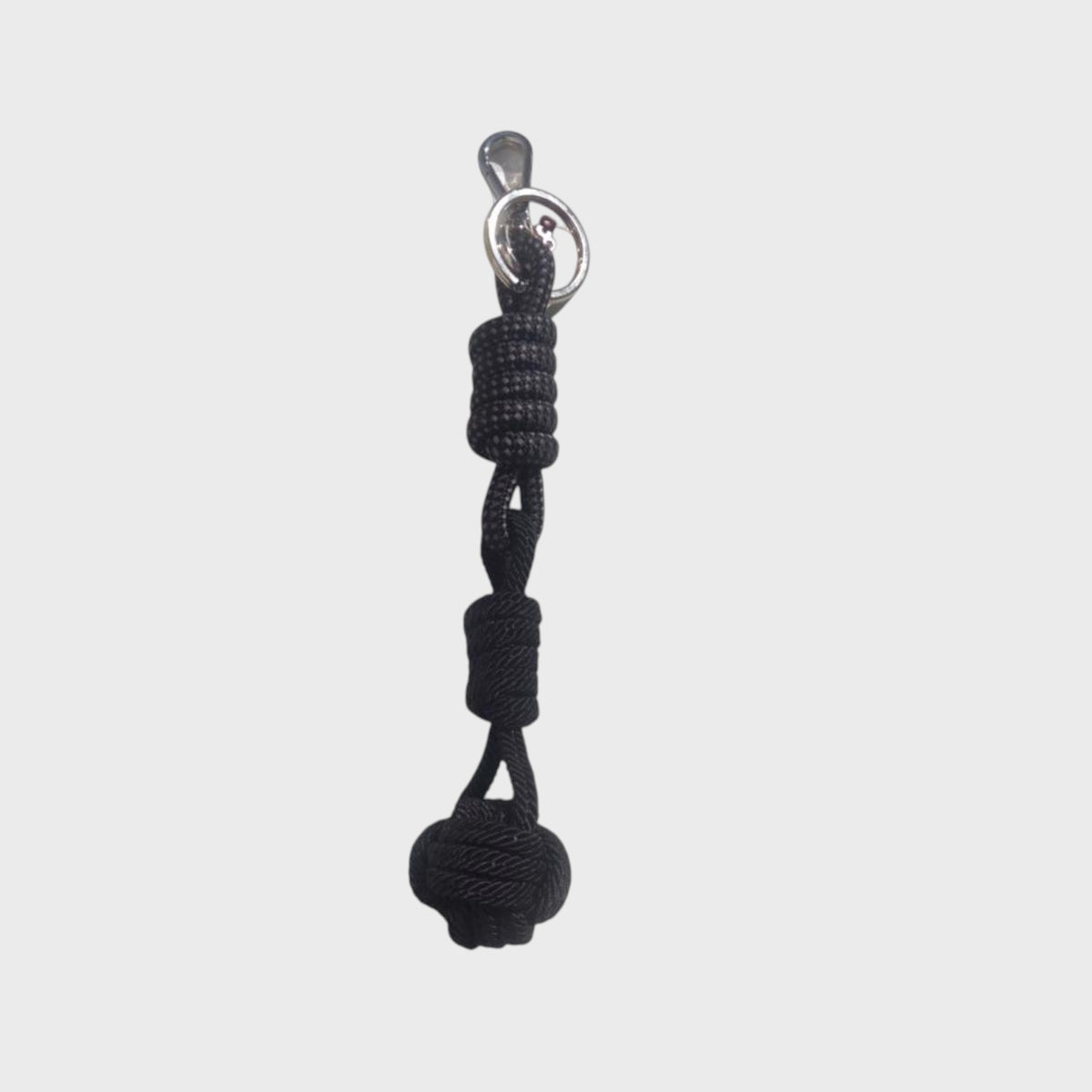 A black macramé keychain finishing in a ball on a grey background.