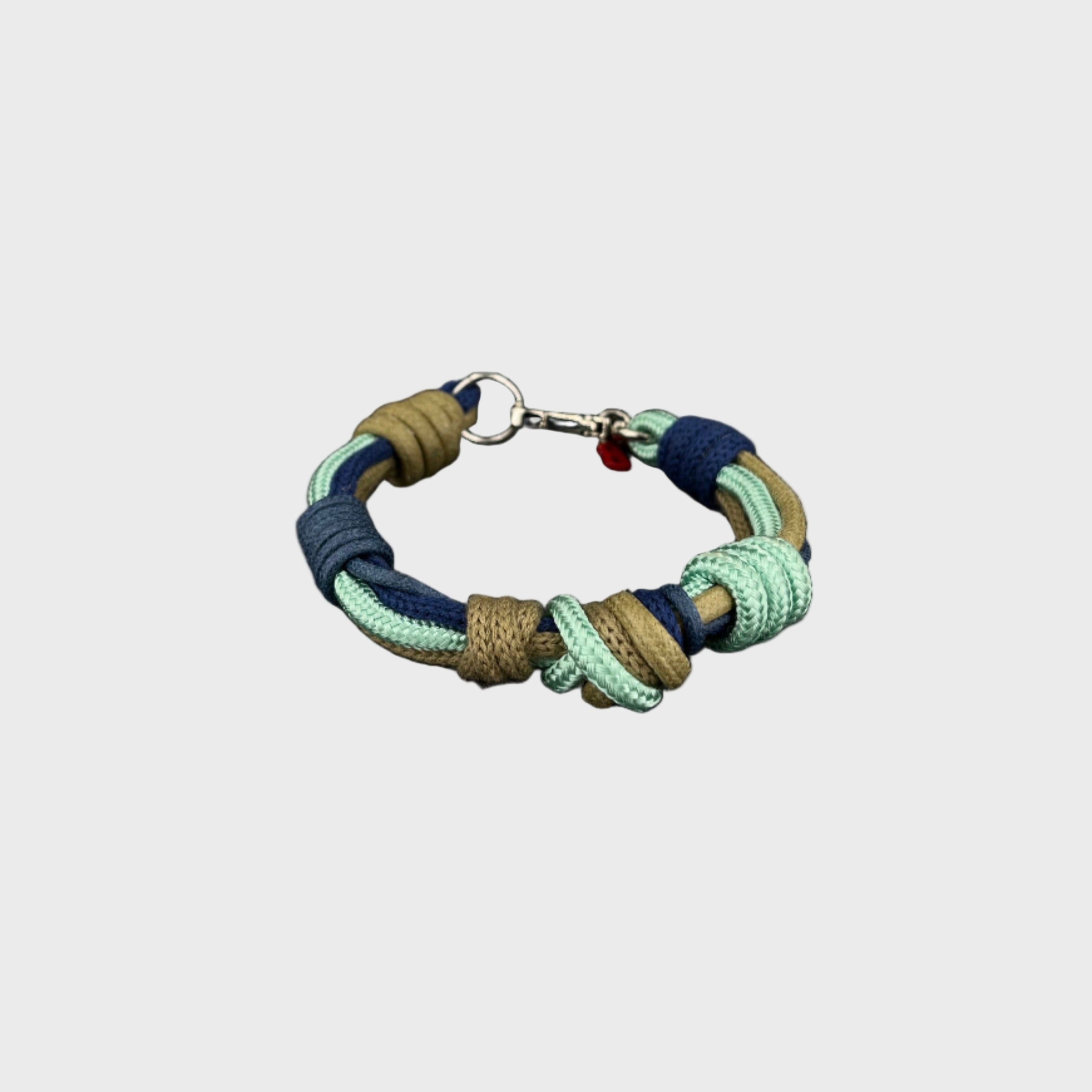 A macramé bracelet with knotted details, featuring shades of blue and green, finished with a silver-tone metal clasp, set on a light gray background.