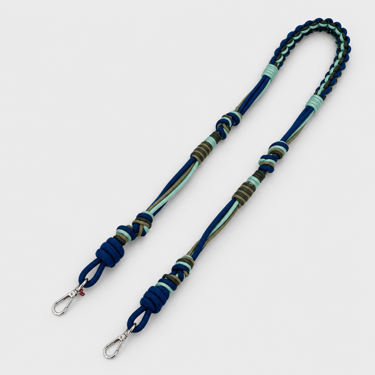 Multicolored braided macramé bag strap in bright blue, dark blue, and green with metal hooks on a light gray background.