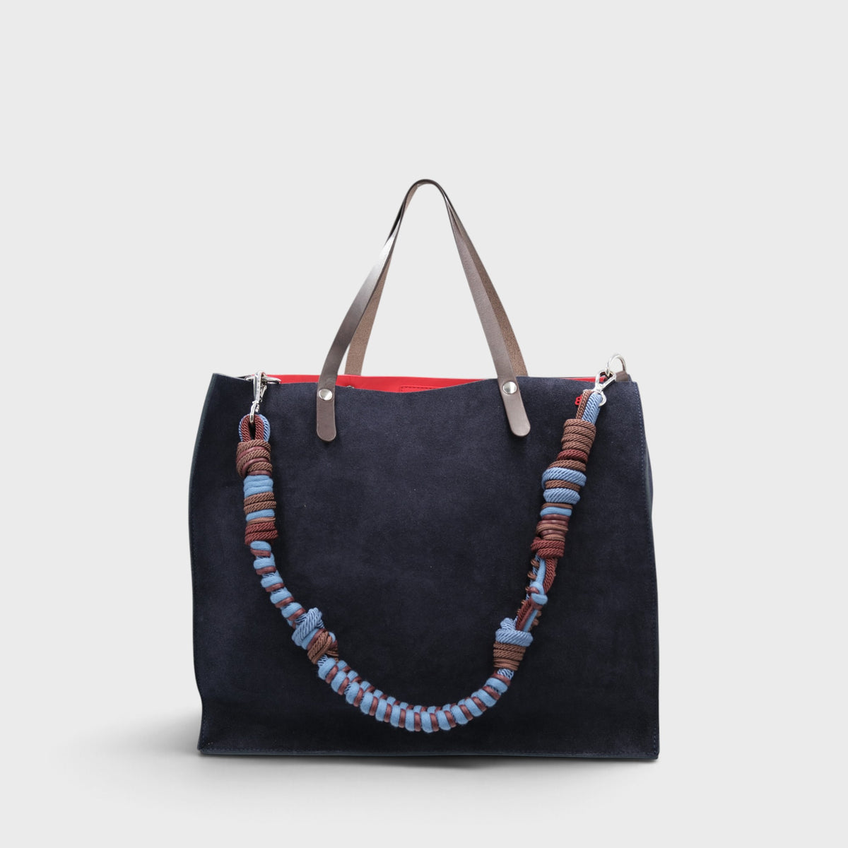 A large dark navy blue suede cabas bag with brown leather handles and a long woven rope shoulder strap in brown, blue, and light blue, shown against a light gray background.