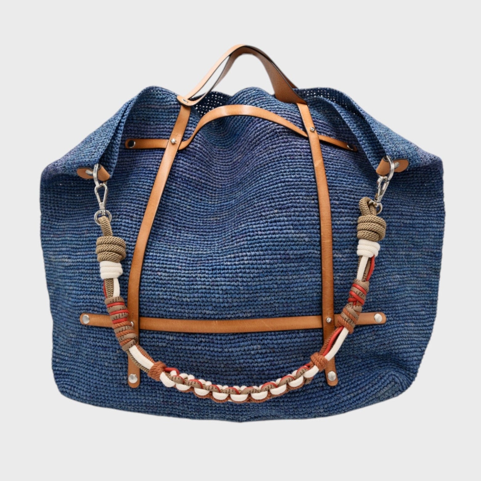 Blue raffia weekend or duffel bag with cognac leather harness and a colourful shoulder strap in white, red and brown.