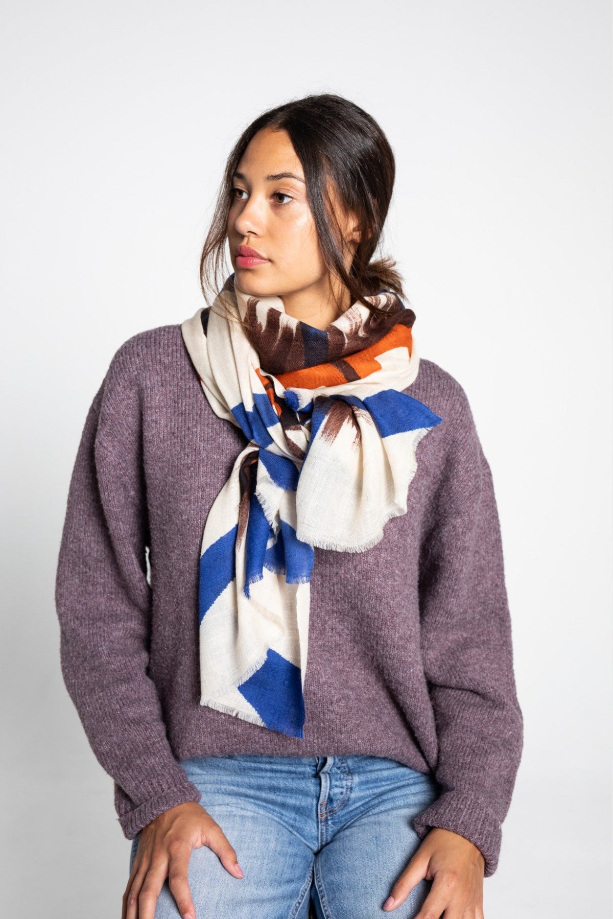 Woman wearing a colorful cashmere shawl as a scarf and purple sweater on a white background