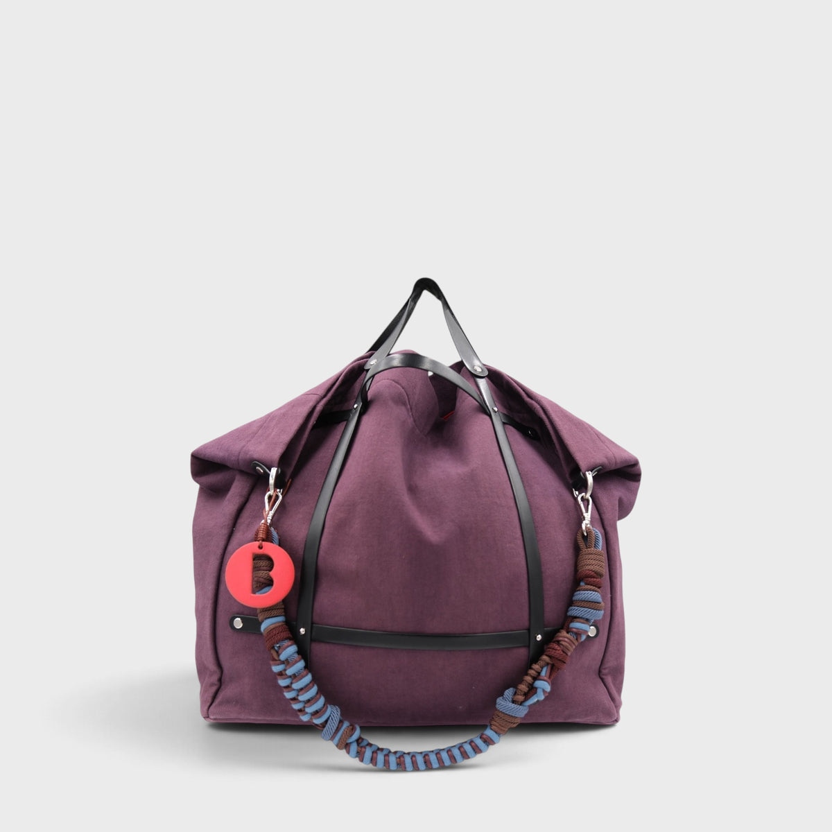 Purple aubergine weekend or duffle bag in canvas with black leather harness, paired with a colourful shoulder strap in blue and brown.