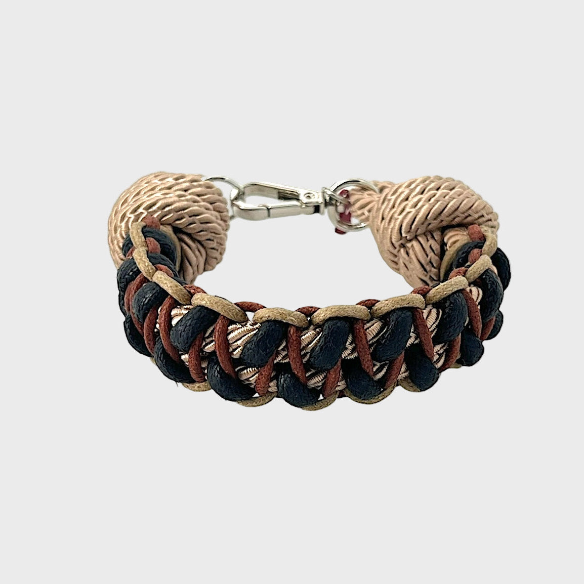 A braided macramé bracelet with shades of beige, black and brown. It ends and a silver clasp, shown on a light gray background.