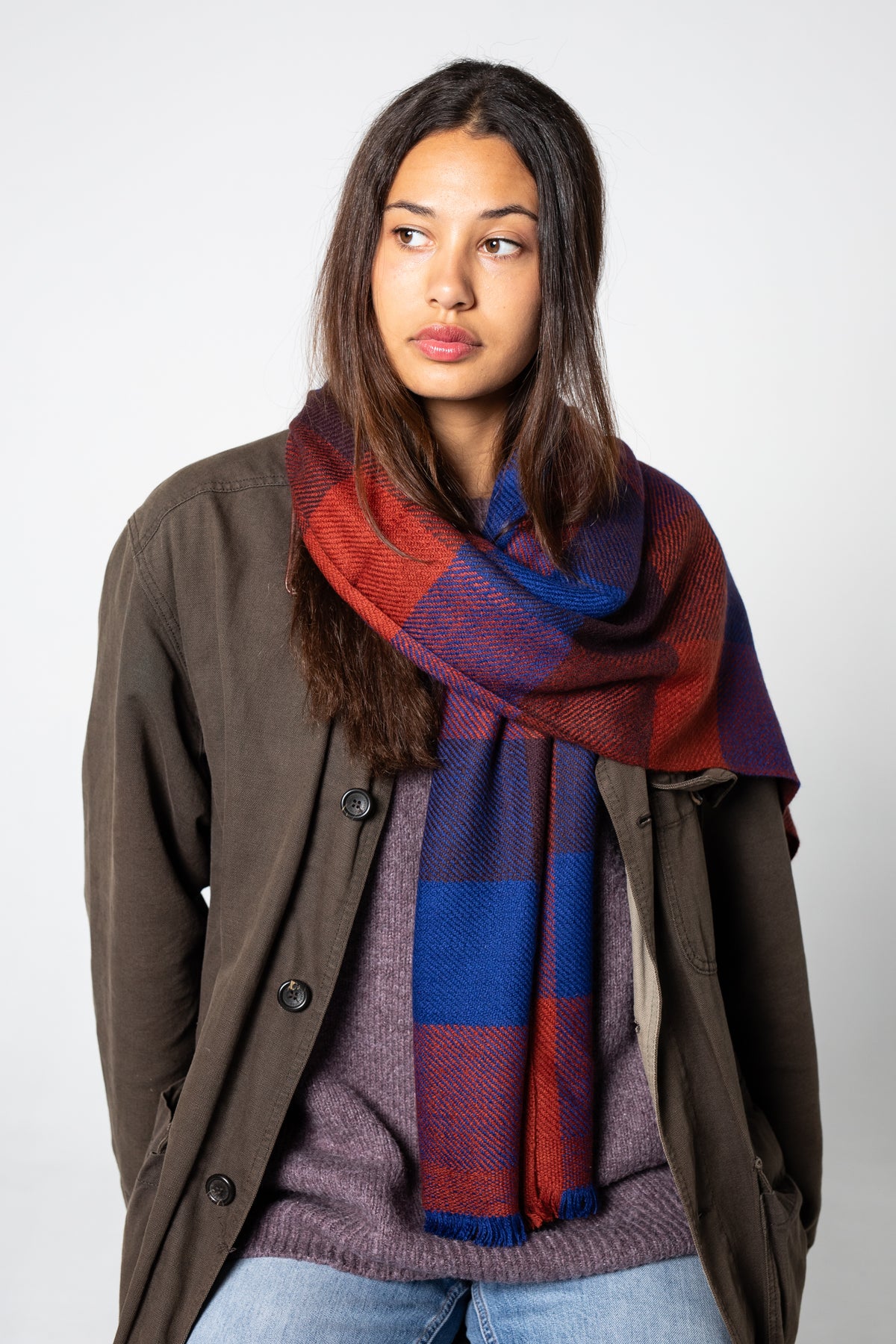 Woman wearing a cashmere plaid scarf with red, blue, and purple colors on a plain background