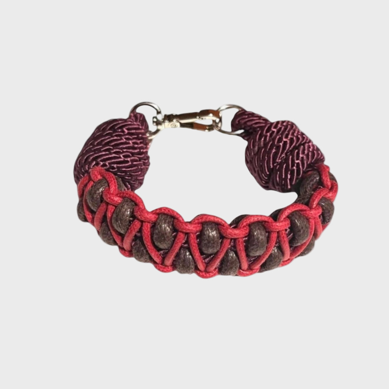 A braided macramé bracelet with shades of brown and brugundy. It ends and a silver clasp, shown on a light gray background.