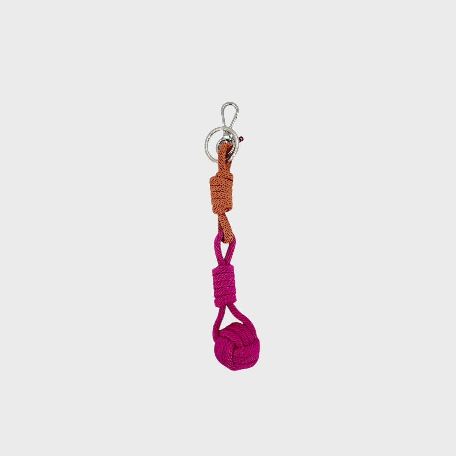 A macramé keychain representing a ball inspired by sailors knots. The straight upper part is warm brown and the ball part is pink.
