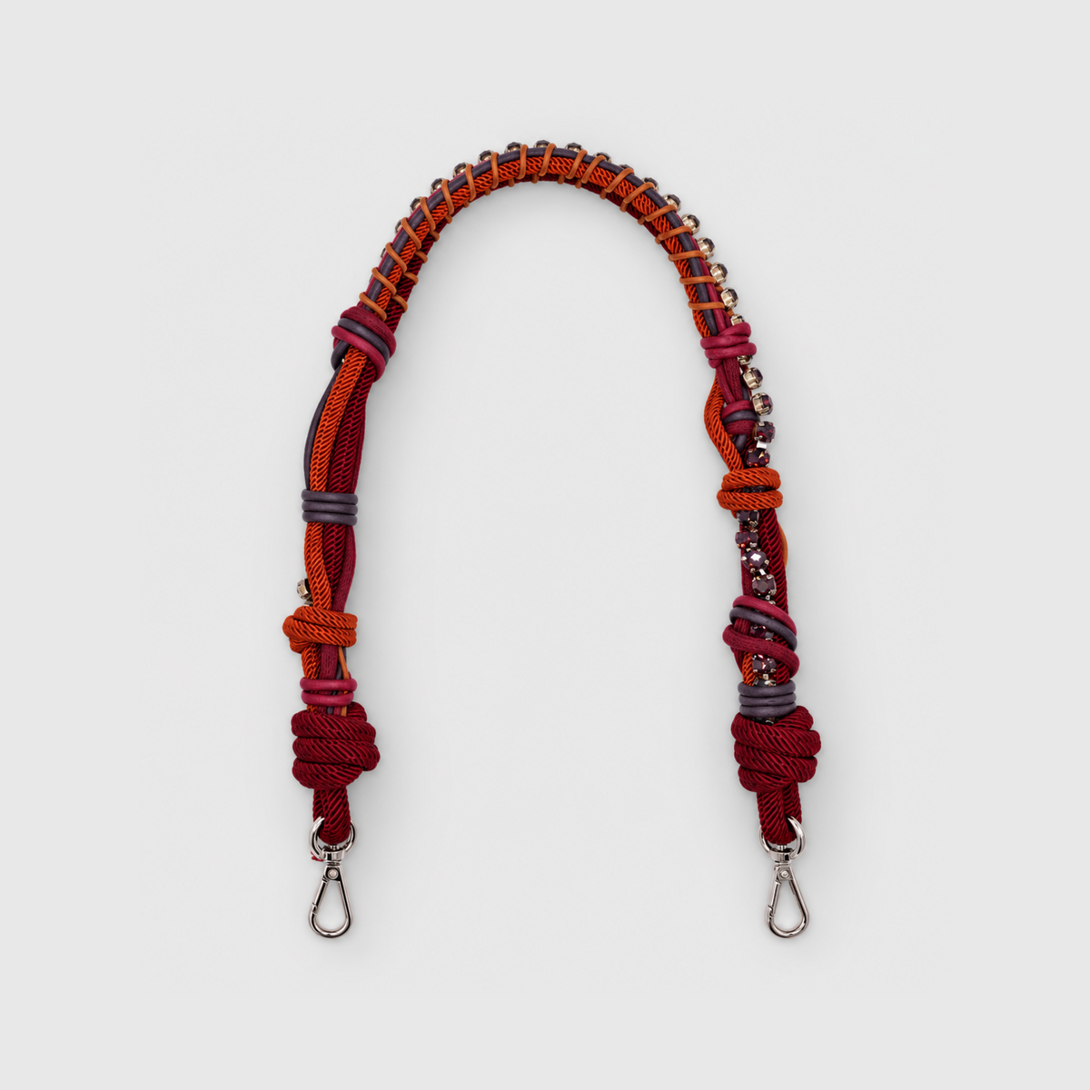Multicolored braided macramé bag strap in burgundy and orange, featuring some purple colored beads and shown on a light grey background.