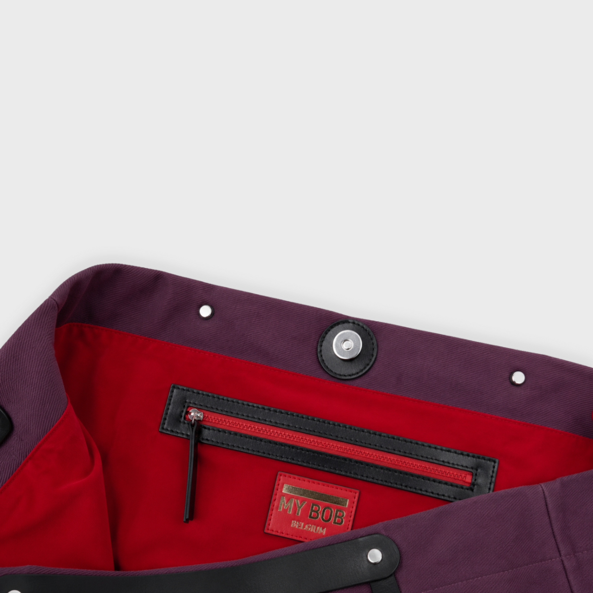 Close-up of a dark purple cotton bag with a bright red interior lining, featuring a black zippered pocket and a red 'MY BOY BELGIUM' brand patch.