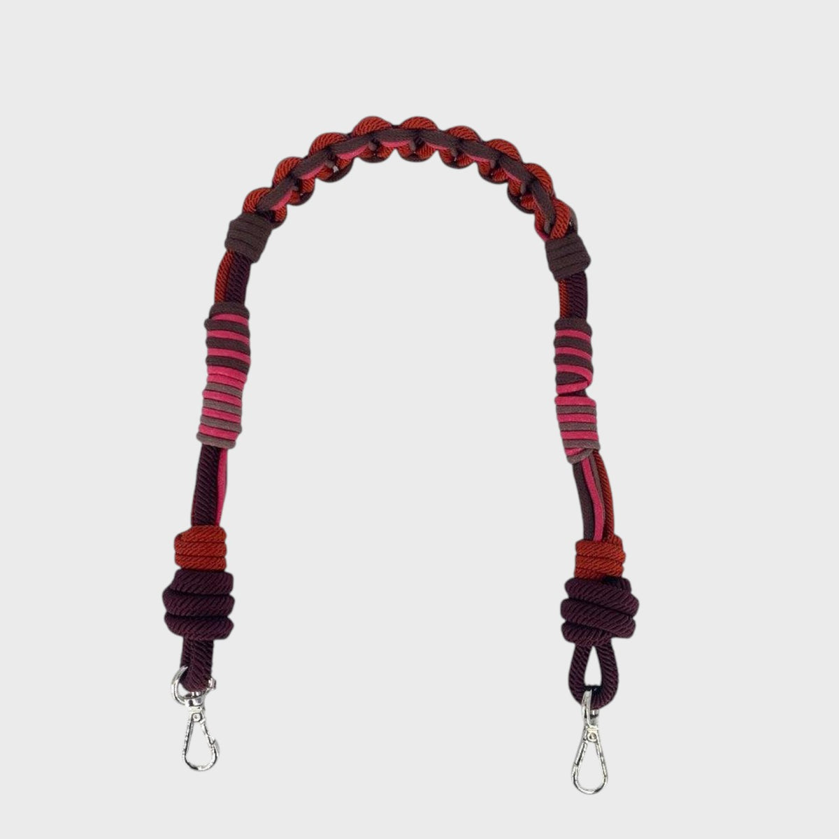 A macramé bag strap with red, pink and brown patterns.