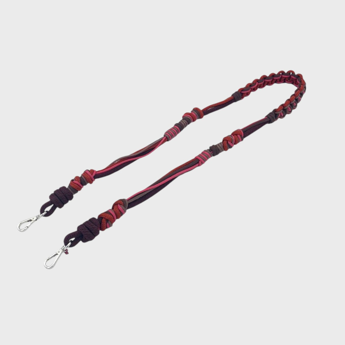 A long macramé bag strap with red, pink and brown patterns.