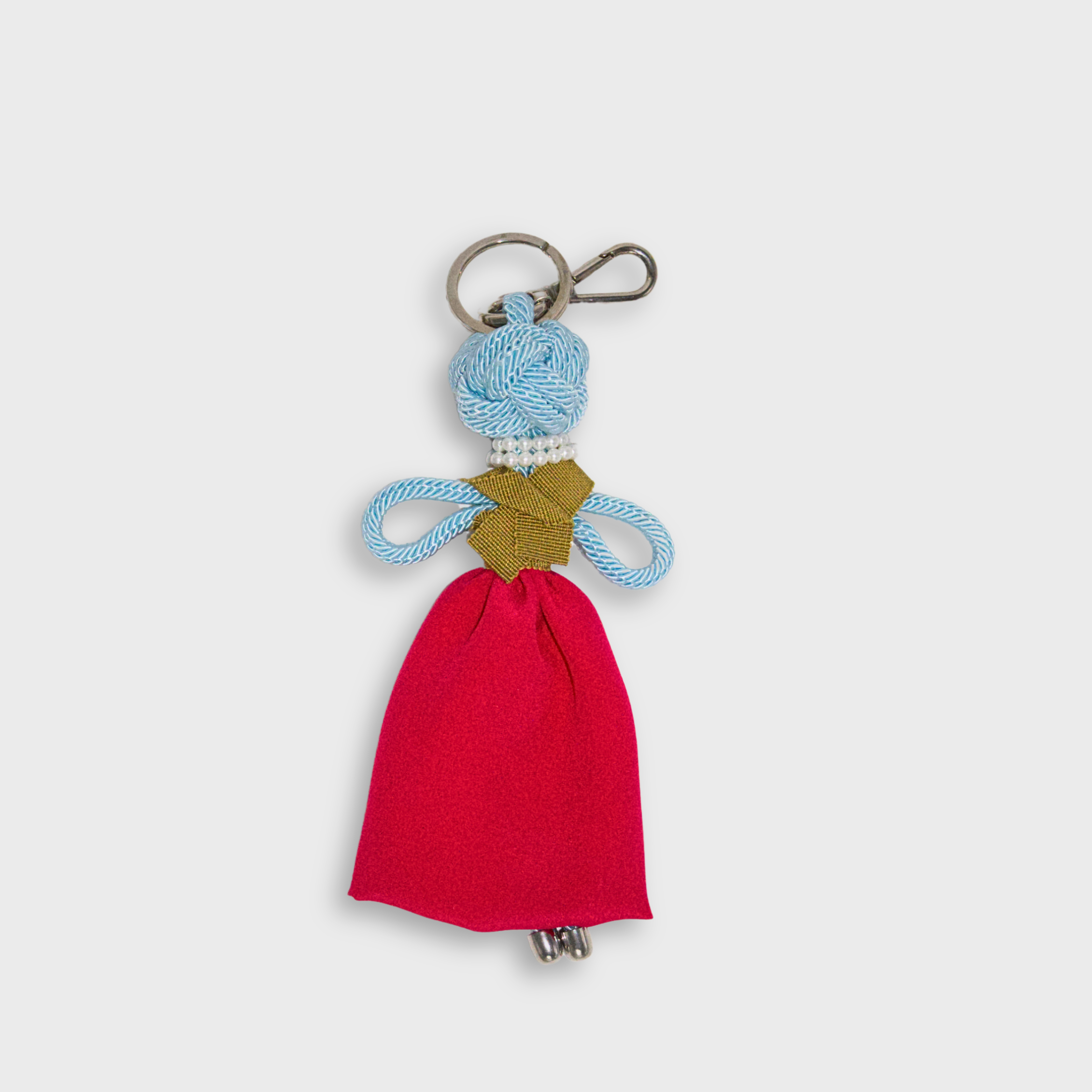 A handmade blue macramé doll keychain featuring a bright pink maxi skirt, a mustard yellow top, a doubled pearl necklace, and a silver metal keyring.