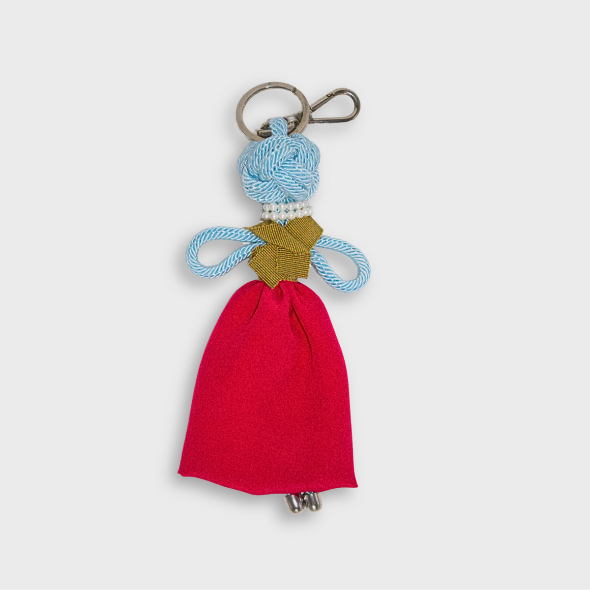 A handmade blue macramé doll keychain featuring a bright pink maxi skirt, a mustard yellow top, a doubled pearl necklace, and a silver metal keyring.