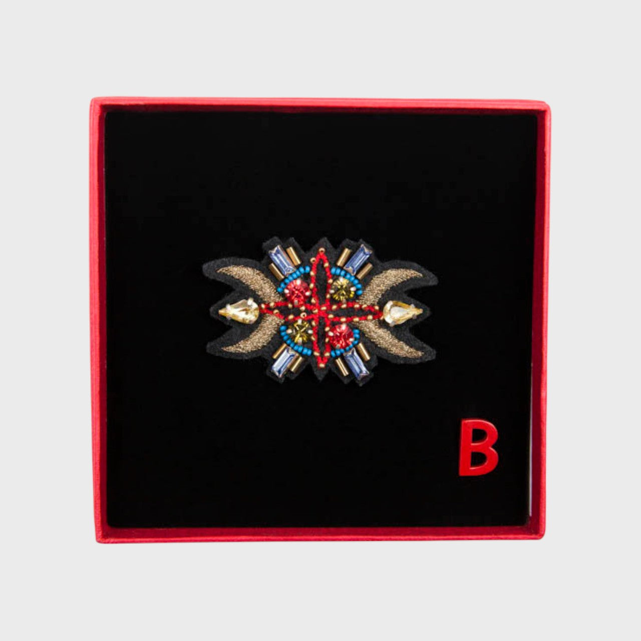 An embroidered brooch representing a sunset horn with gold details in a box.