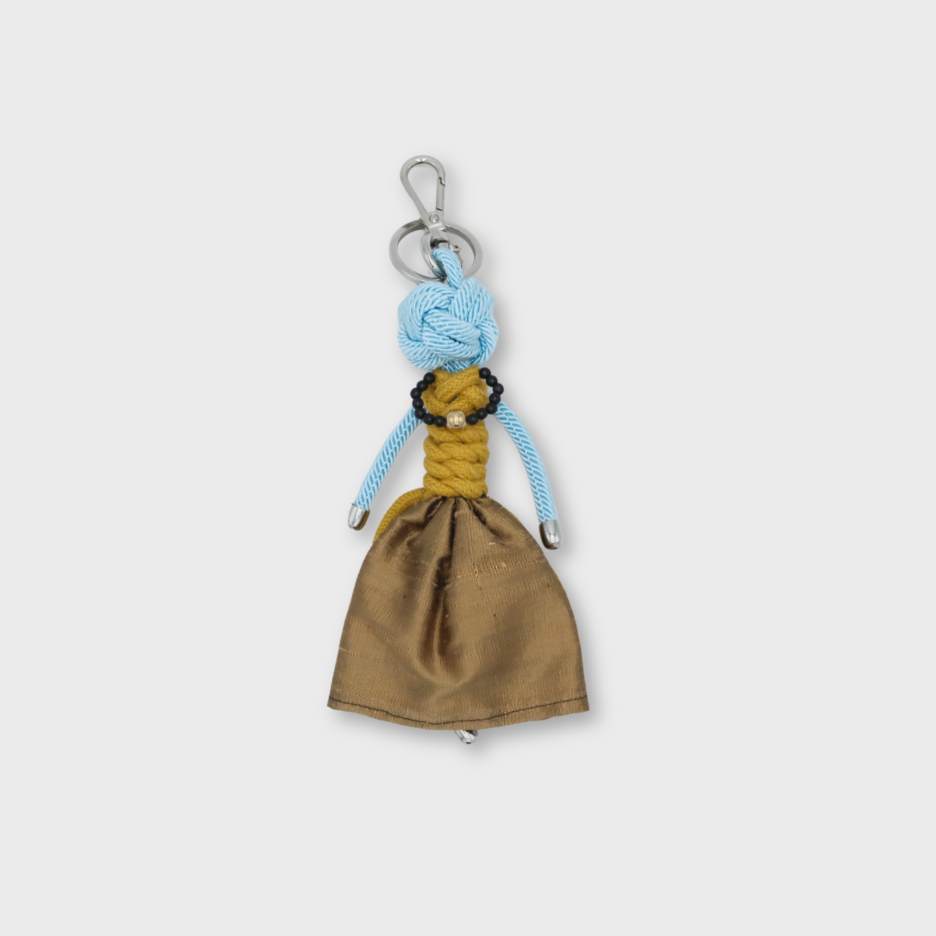 A handmade keychain doll with a light blue knotted rope head, yellow braided rope torso, and a brown fabric skirt, attached to a silver metal key ring.