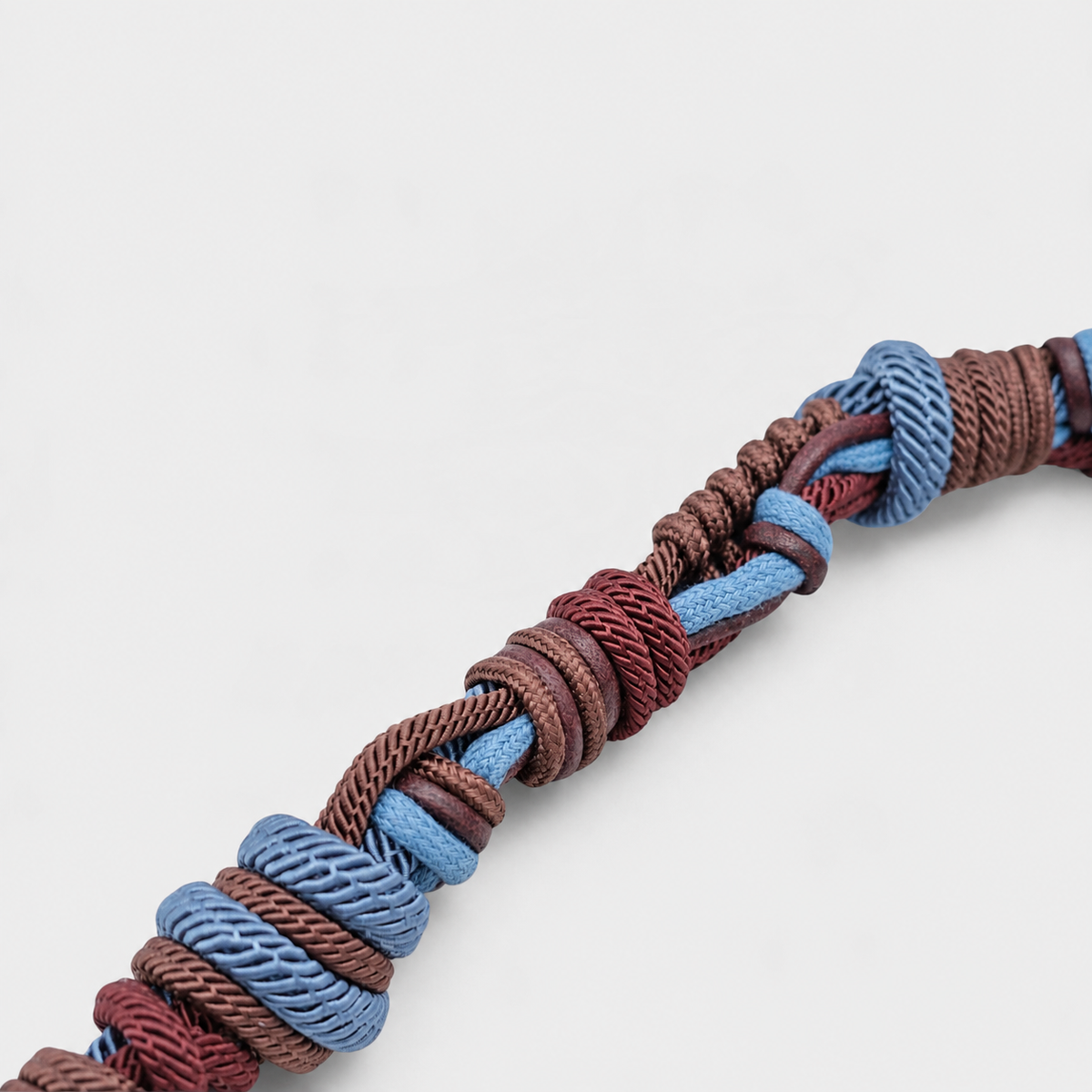 A close-up of a braided macramé bag strap, featuring interwoven brown, burgundy, and light blue cords on a clean white background.