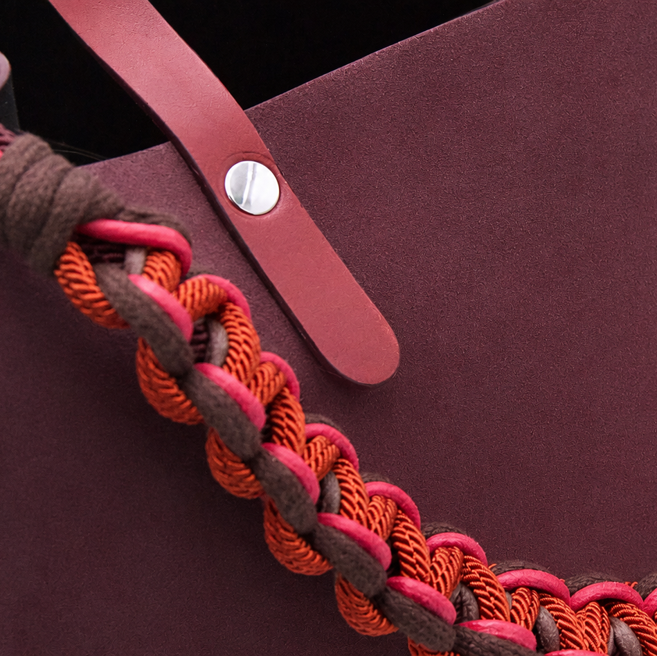 Close-up of a burgundy suede leather cabas bag featuring a thick macramé shoulder strap in orange, pink, and dark brown.