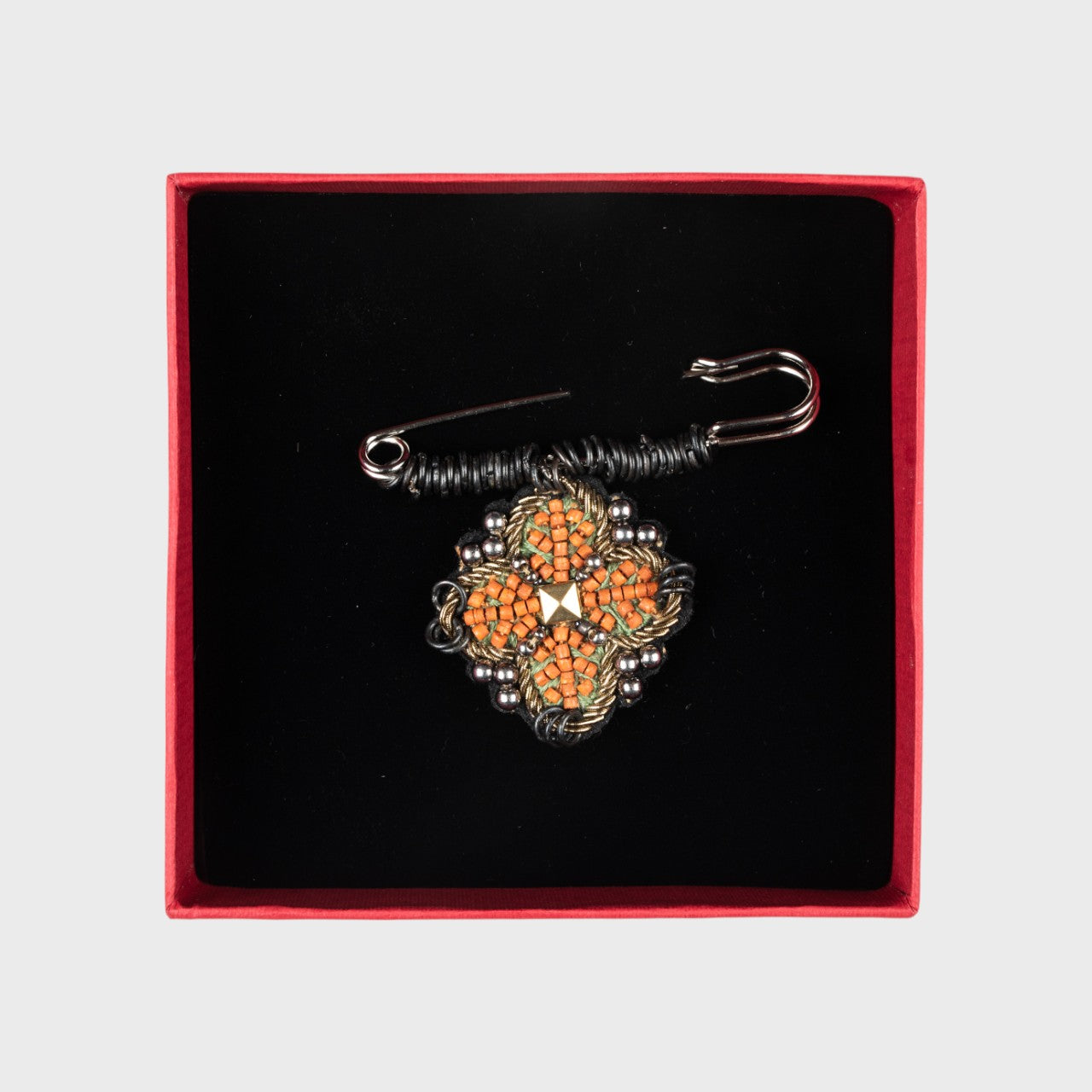 An embroidered pin with orange details in a box.
