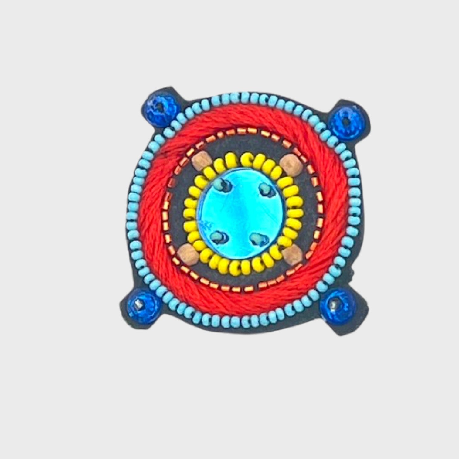 An embroidered brooch representing a compass with a blue center and blue, yellow and red details.