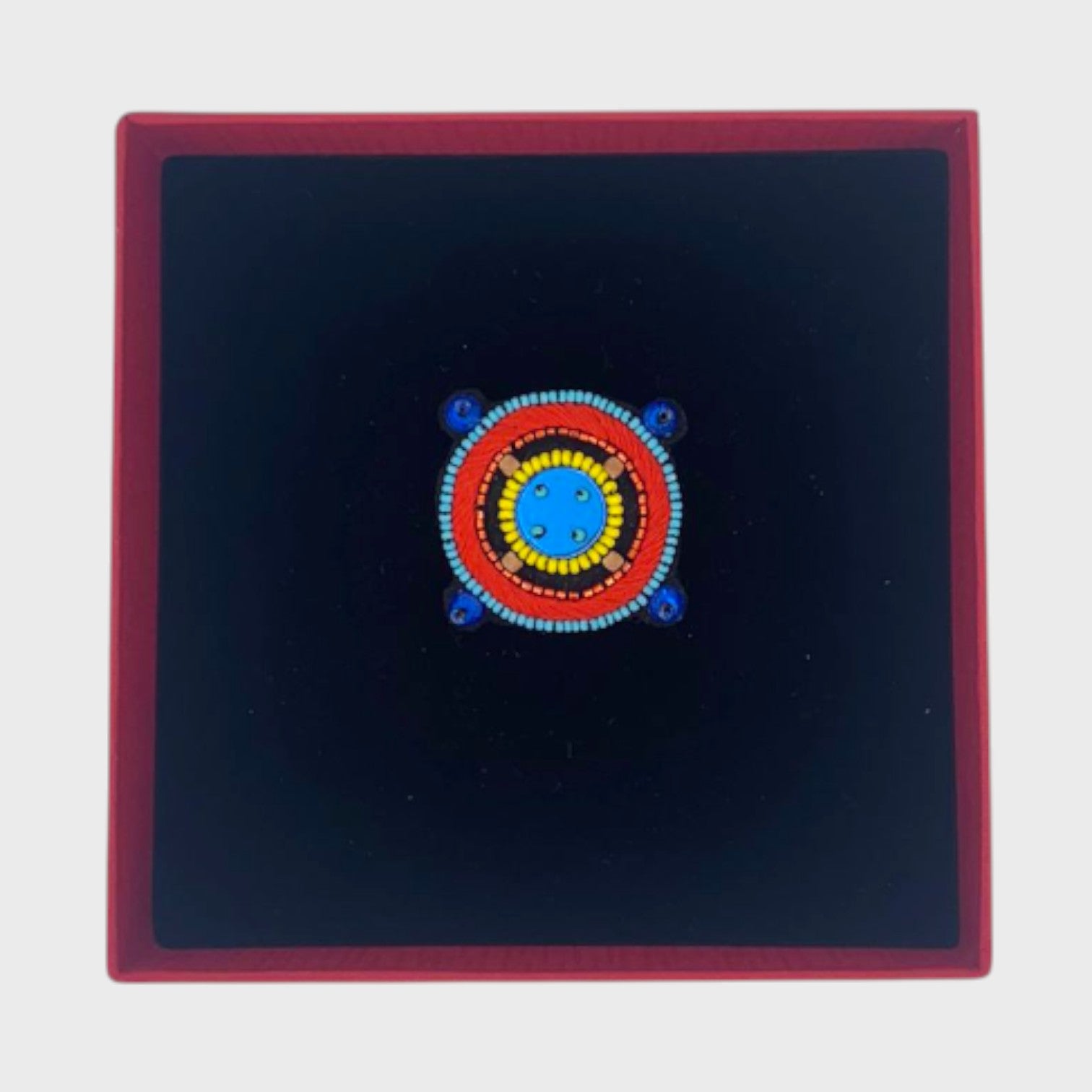 An embroidered brooch representing a compass with a blue center in a box.