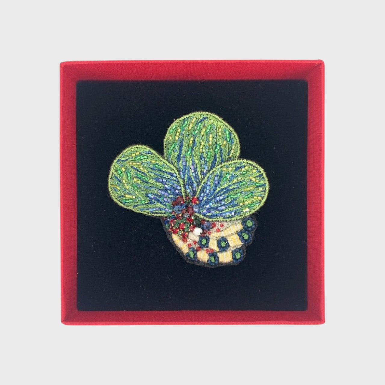 An embroidered brooch representing coral leaves in a box.