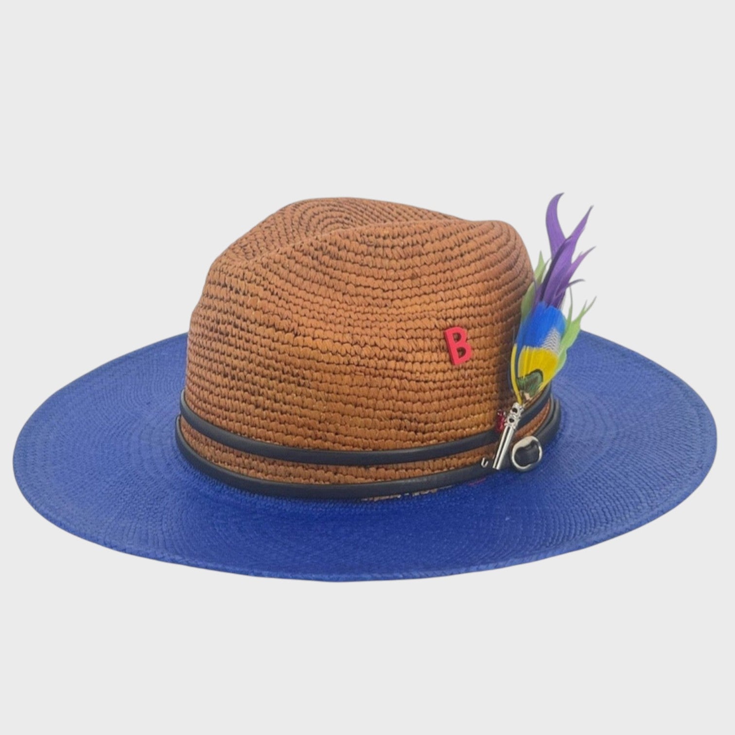 A brown and dark blue raffia hat with a double black leather band around it and a yellow, blue, green and purple feather brooch pinned on it.