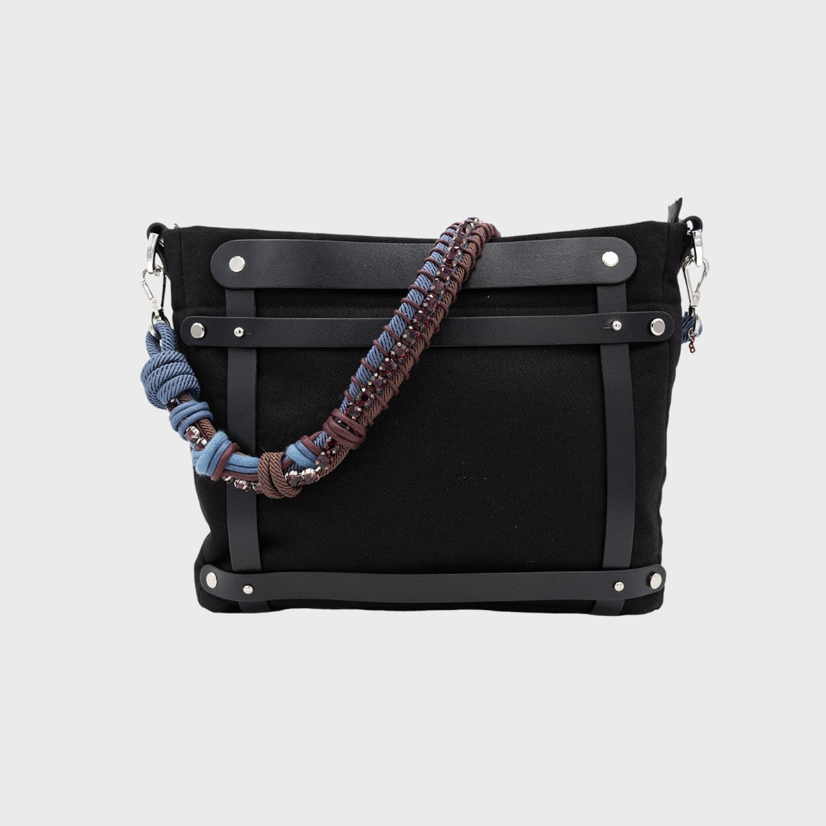 Black handbag with a colorful strap wth brown and blue macramé and purple rhinestones on a light gray background