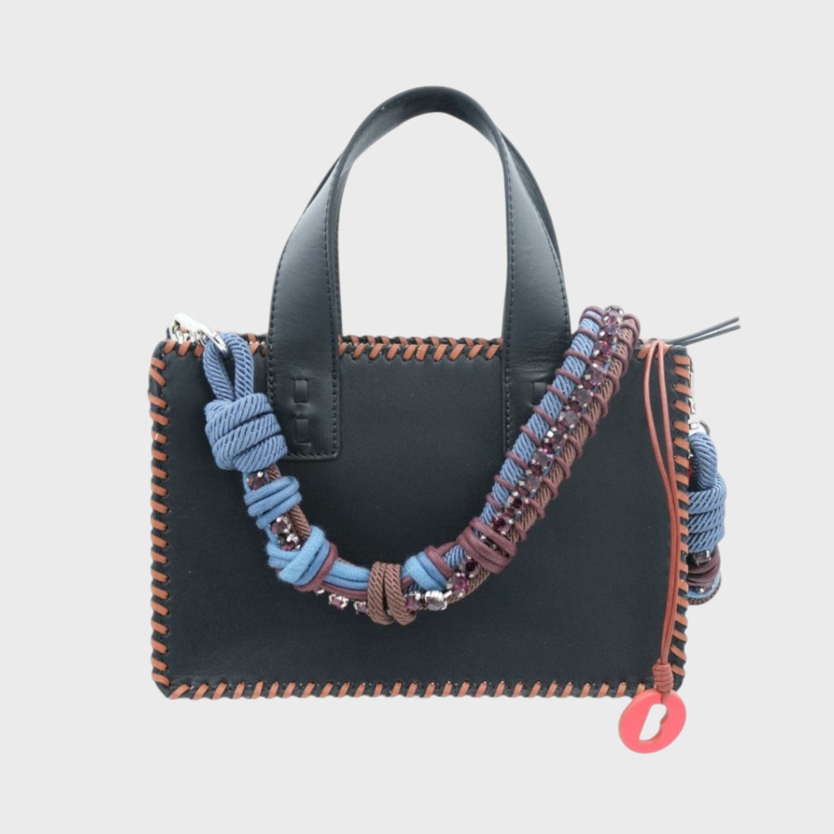 Black handbag with colorful braided bag strap with brown and blue macramé and purple rhinestones on a light gray background