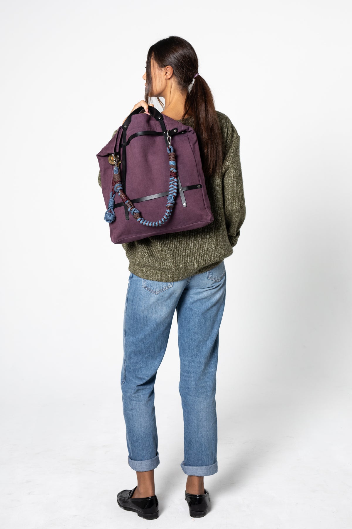 Person wearing a purple bag with a decorative blue and brown macramé bag strap on a white background