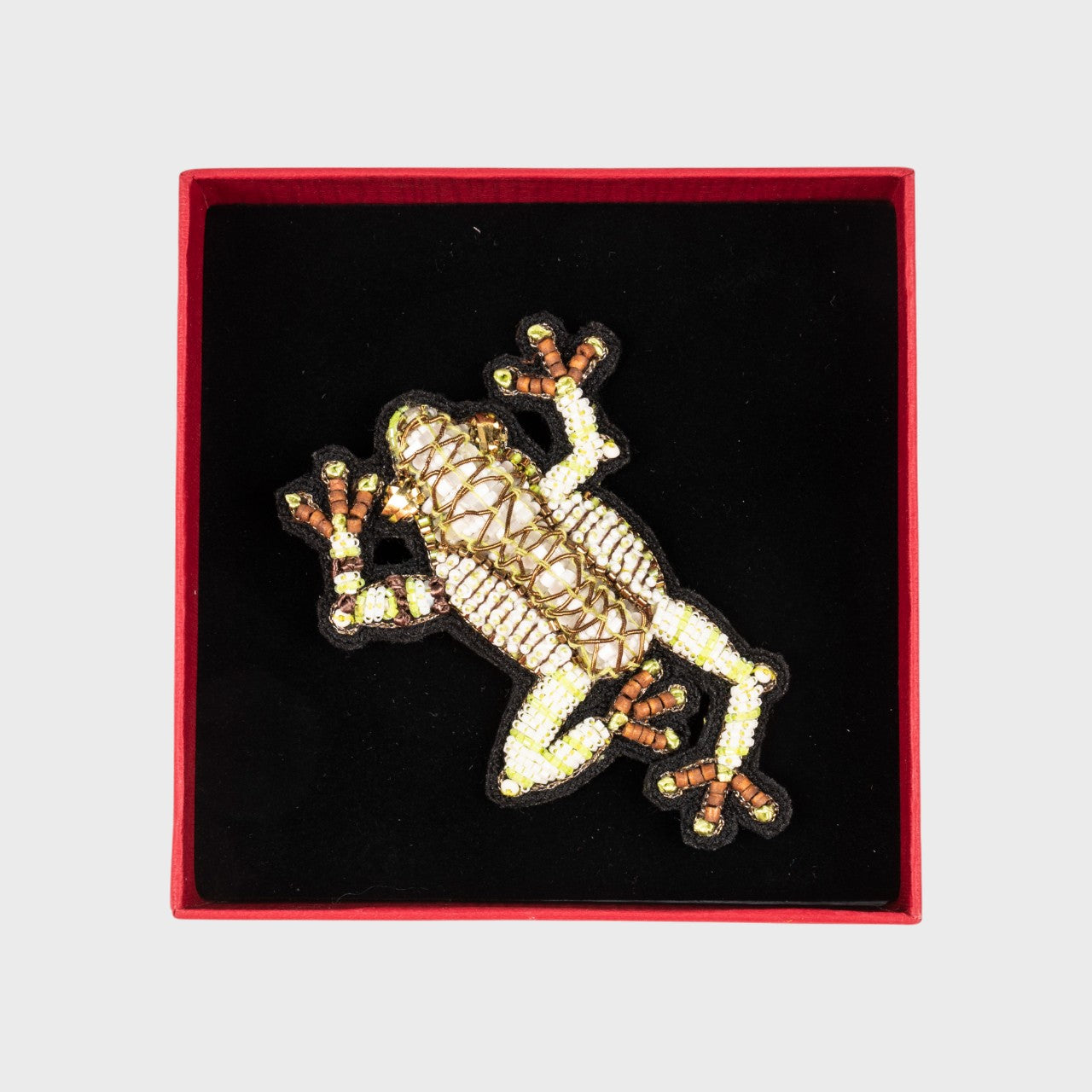An embroidered brooch representing a green dendrobate in a box.