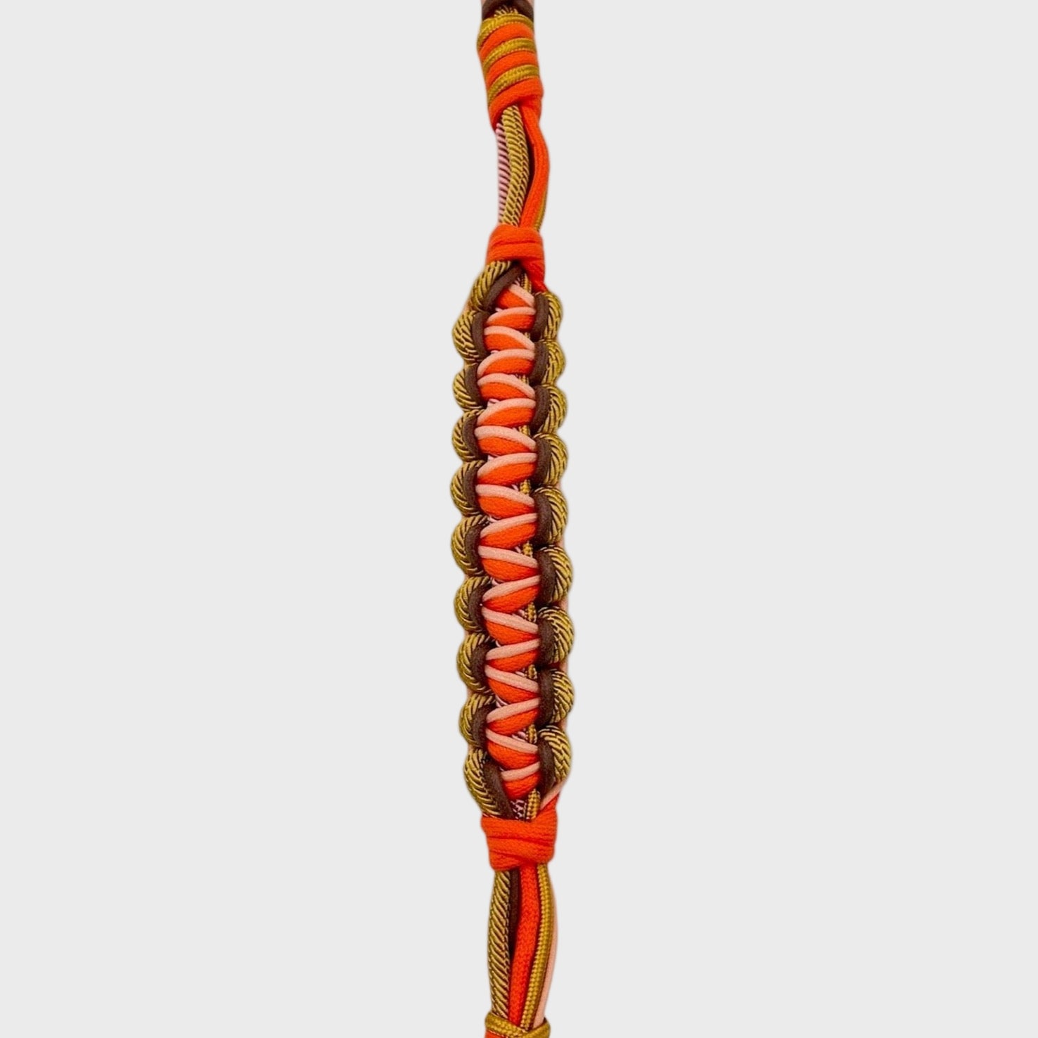 A close up of the multicolored braided macramé bag strap in orange, soft pink, and soft yellow with metal hooks on a light gray background.