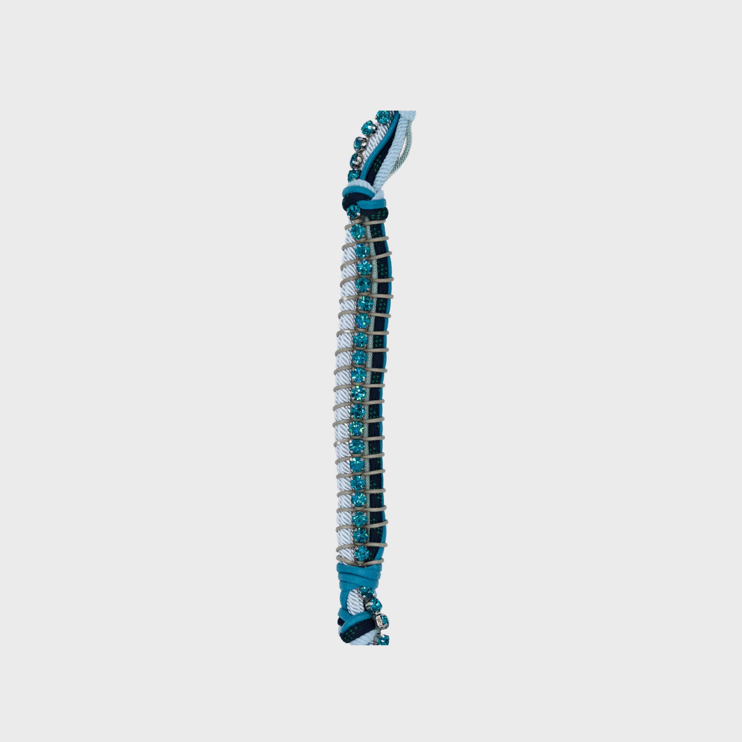 Close up of the multicolored braided macramé bag strap in various blues, featuring some blue colored beads and shown on a light grey background.