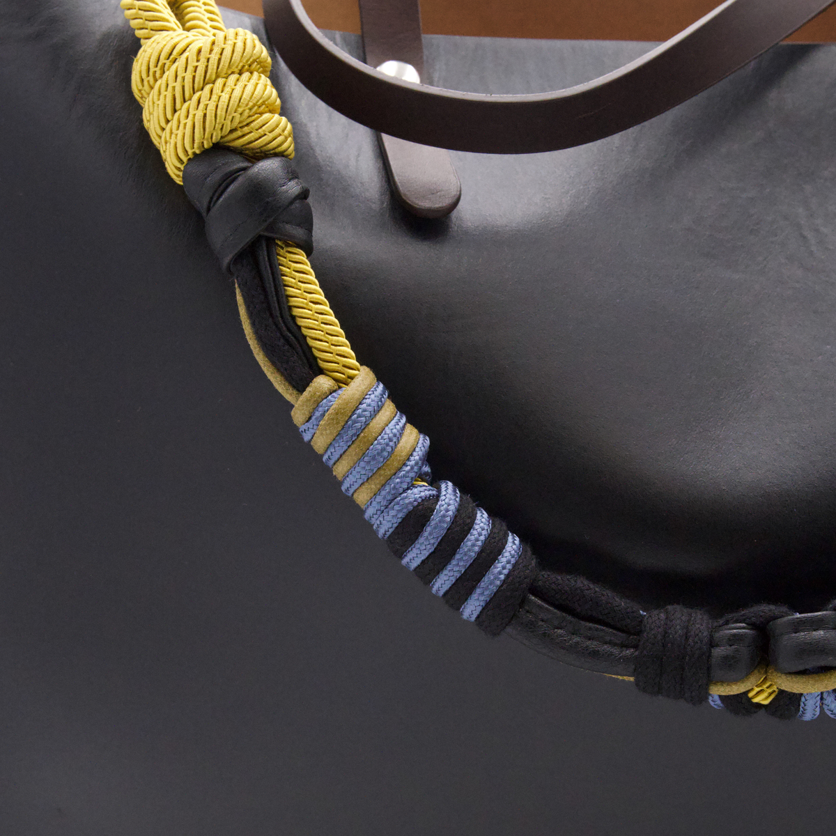 Close-up of a black leather macrame shoulder strap featuring a thick braided yellow rope handle and a black leather wrap with blue and yellow striped cord accents.