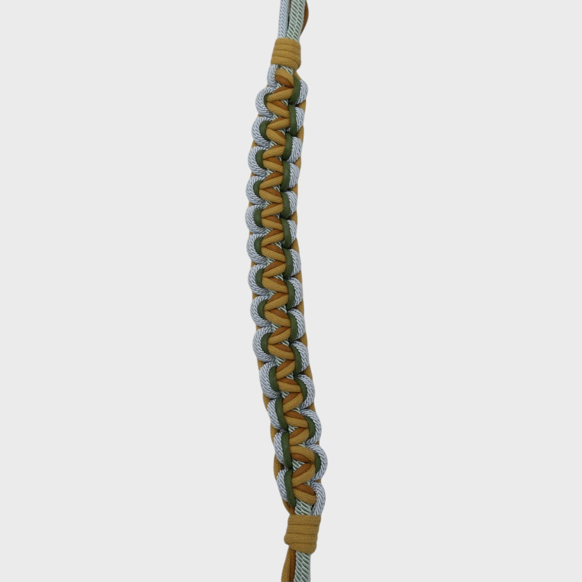 An up close photo of a multicolored braided macramé bag strap in yellow, light blue, and green with metal hooks on a light gray background.