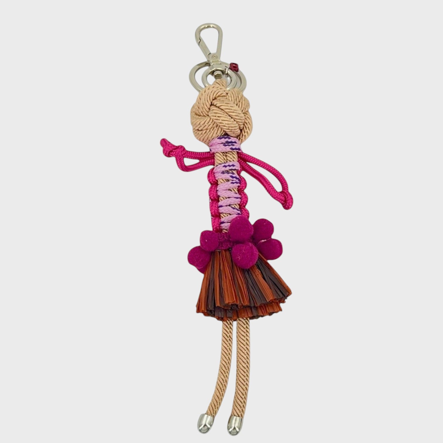 Handmade macramé bag charm featuring an exotic character wearing a short brown fringed skirt and a fun pink belt. She is attached to a silver clasp.