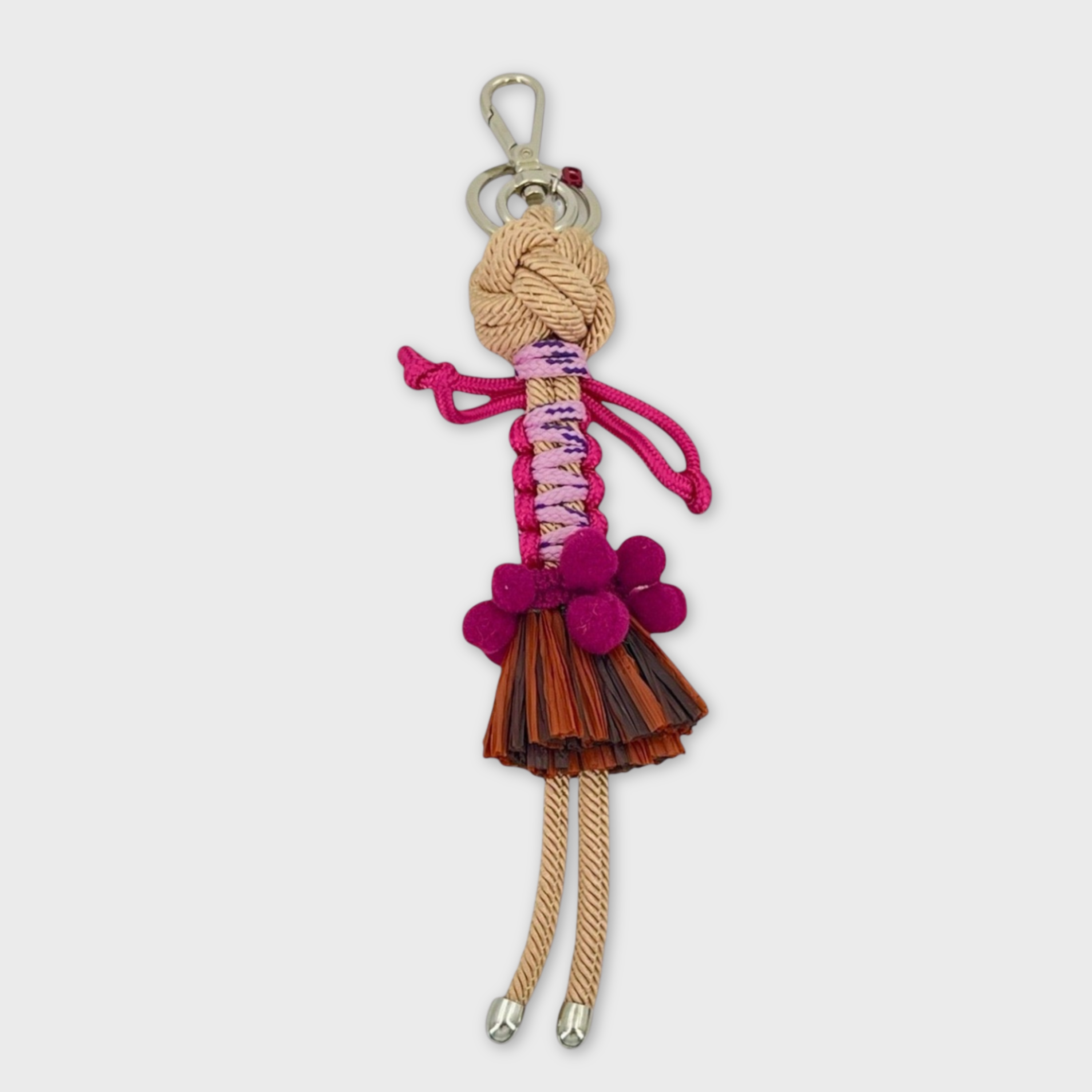 Handmade macramé bag charm featuring an exotic character wearing a short brown fringed skirt and a fun pink belt. She is attached to a silver clasp.