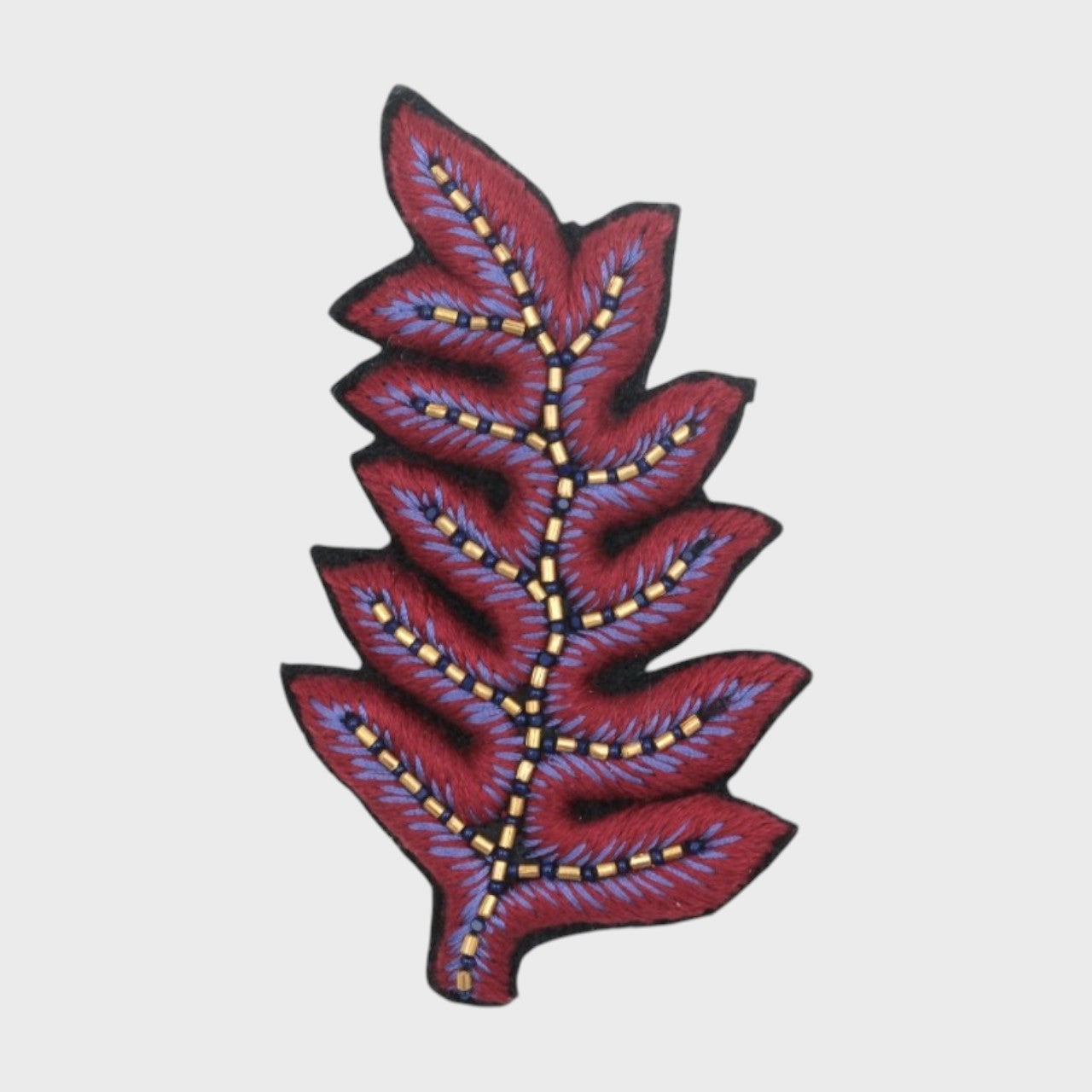 An embroidered brooch representing a fern leave with purple and burgundy details.