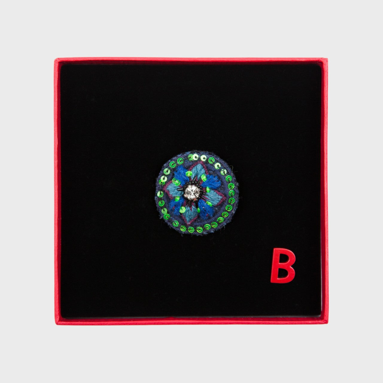 An embroidered brooch representing a blue flower in a box.