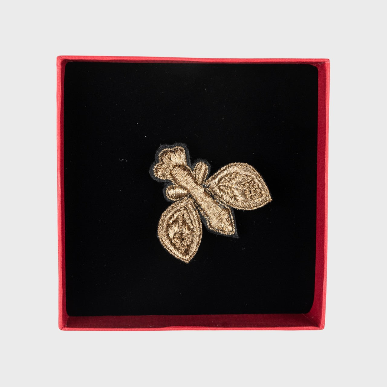 An embroidered brooch of a golden fly in a box.