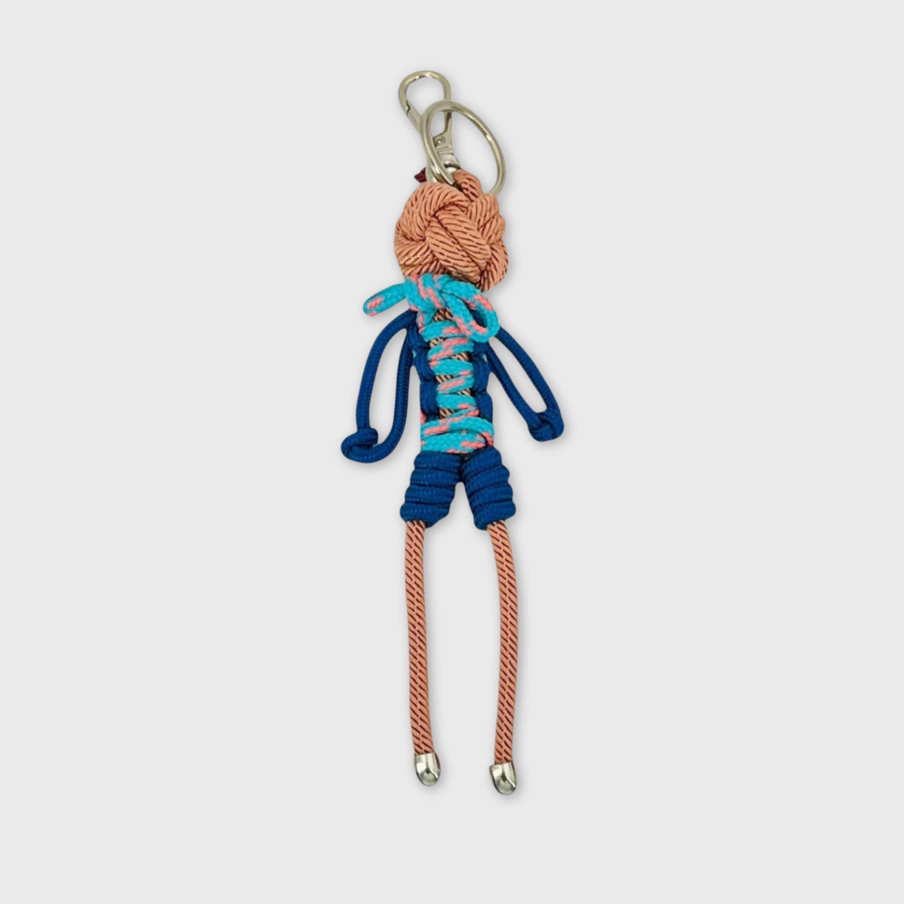 Handmade tan macramé bag charm featuring a male character, wearing short overalls in different shades of blue. He is attached to a silver clasp.