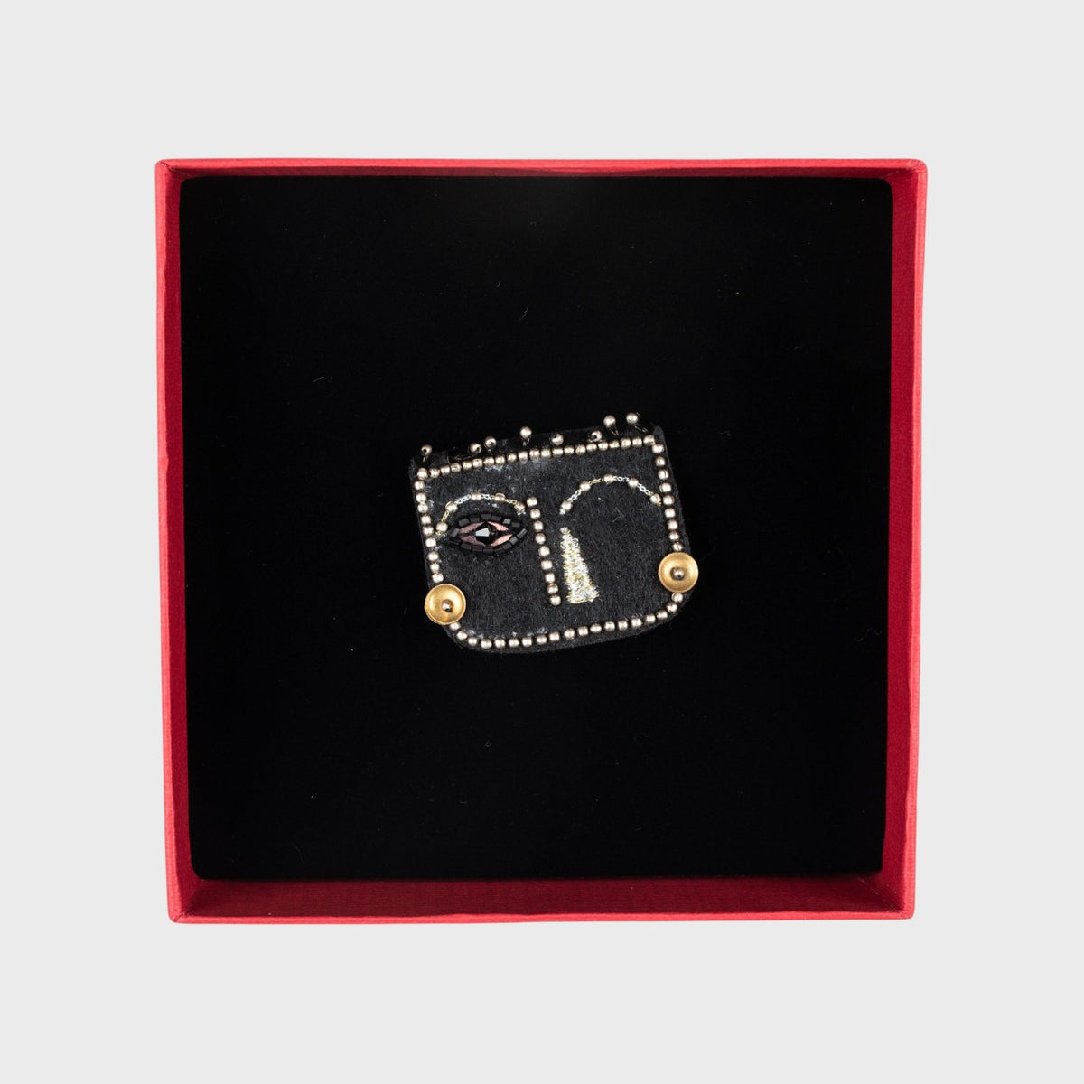 Black brooch with gold accents on a black velvet in a red box