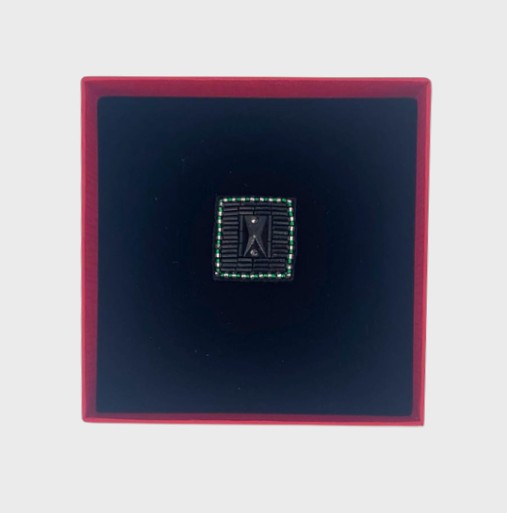 An embroidered brooch representing a button in a red box.