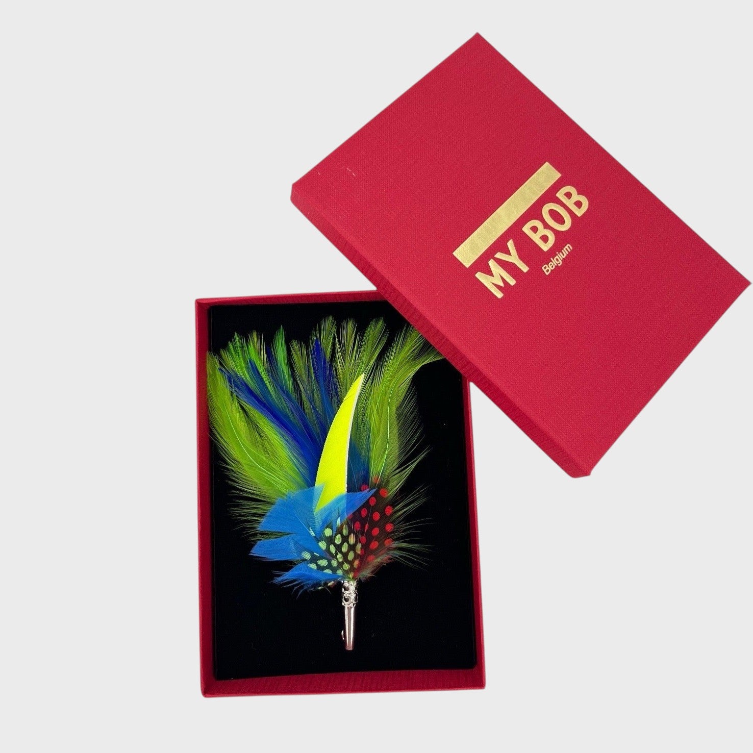 Green, blue and yellow feather brooch in a box on a light gray background