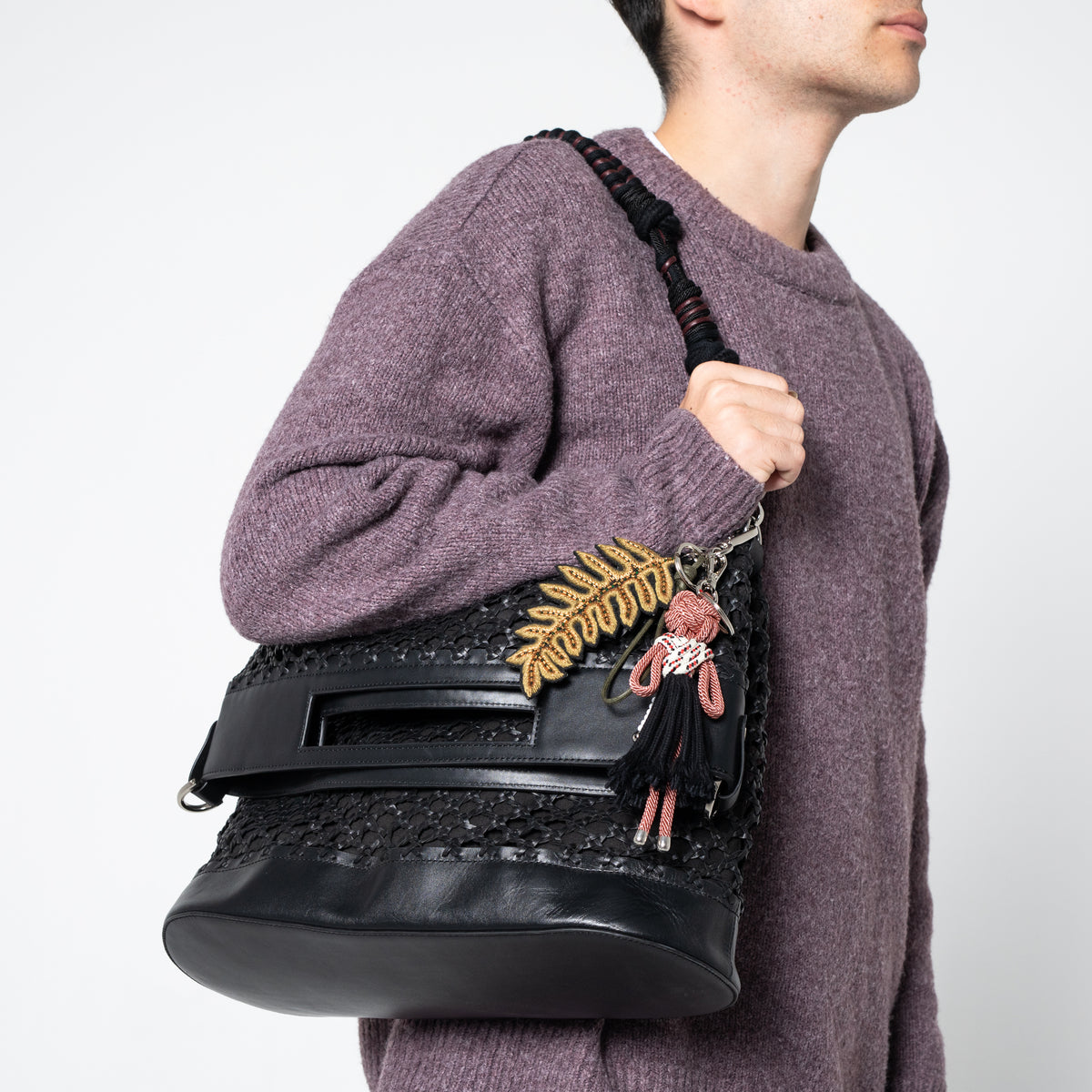 Person wearing a black textured bag with a green embroidered fern leave on a plain background